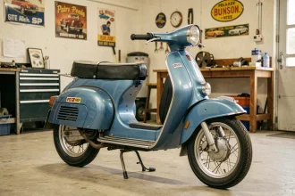 Peugeot 103 SP bleu d'origine en parfait état dans un garage vintage, vue 3/4 mettant en valeur la carrosserie bleue métallisée et les détails chromés