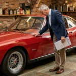Propriétaire examinant une Ferrari ancienne des années 60 dans un garage privé en pierre, tenant un dossier d'assurance pour voiture de collection