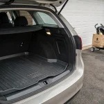 Coffre de Peugeot 308 SW ouvert avec tapis de protection anthracite ajusté et bords relevés, vue arrière trois quarts